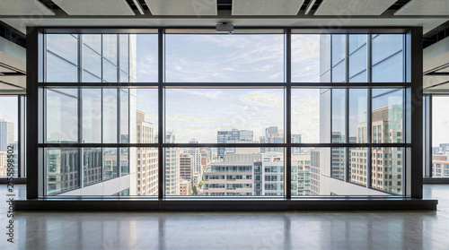 Modern empty interior atrium with large glass facade window, dark metal framing and polished concrete floor. Commercial office building window wall with daylight and urban cityscape view