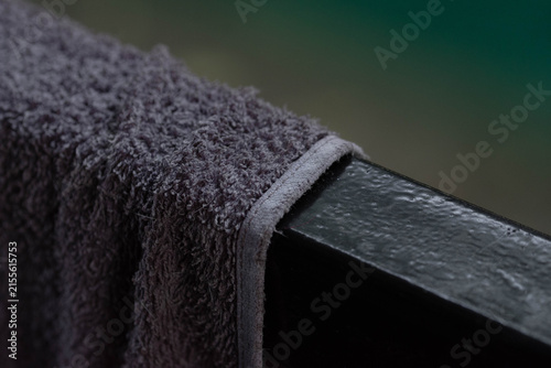 Macro close-up of a dark gray terry cloth towel draped over a wet, glossy black railing against a blurred green background