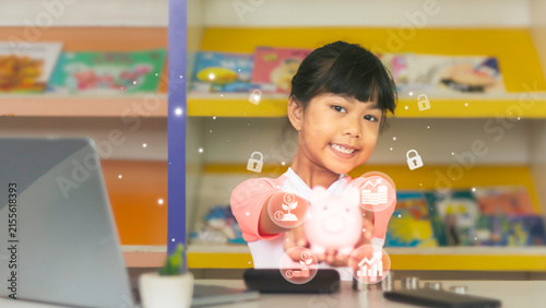Asian girl showing pink piggybank with digital security and investment overlay icons at desk