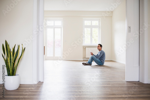 Young man in new home sitting on floor with tablet