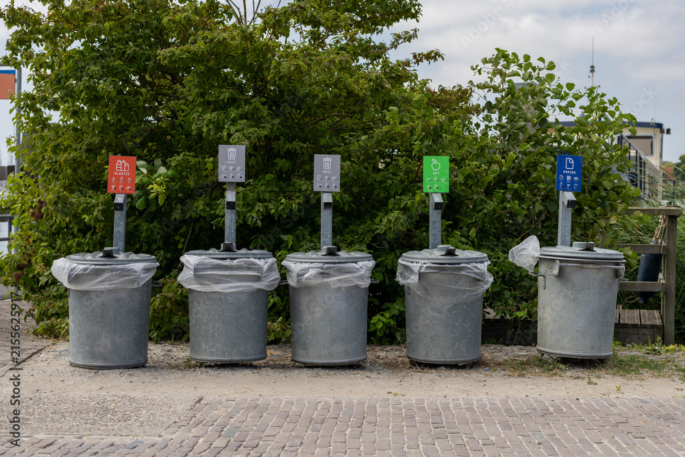 Obraz premium Row of outdoor recycling bins for separate waste collection, with signs for plastic, residual waste, glass and paper against a green natural background.