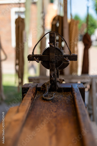 Close-up of an old rope making tool with metal hooks, gears and a wooden frame, showing traditional craftsmanship and rustic textile work with soft background blur.