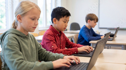Diverse group of school children sitting at desks and typing on laptop computers in classroom