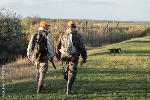 A hunters in camouflage clothing with a gun in his hands walks along the reeds.