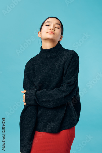 Young woman in black sweater and red skirt posing with folded arms on blue background. Casual outfit  confident expression  indoor studio portrait with minimalistic style and soft lighting.