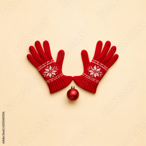 Minimalist conceptual Christmas stock photography, two red knitted Christmas gloves arranged symmetrically and small round red ornament positioned between them to resemble the antlers of a reindeer