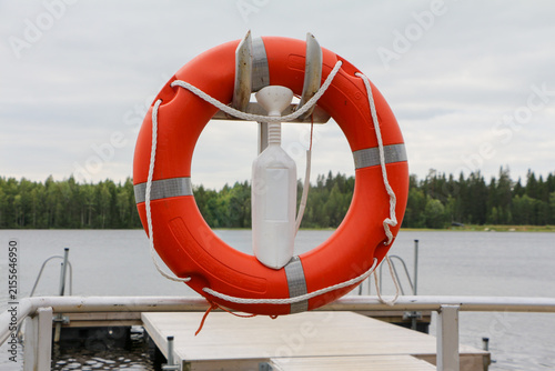 Obraz na plátne Red and white lifebuoy hanging on a metal stand beside a lake dock, showing esse