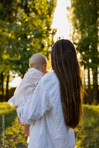 Fotografie Mother holding her baby in a sun-drenched park during golden hour