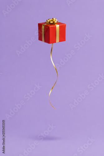 Minimalist conceptual of a single beautifully wrapped red Christmas gift box floating in mid-air like a helium balloon