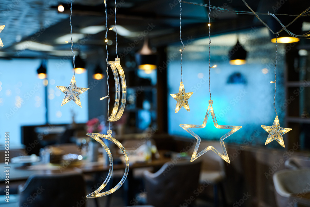 Obraz premium Hanging Star and Moon Christmas Lights Decoration in Cozy Restaurant Interior With Festive Bokeh