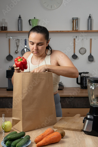 Woman in sportswear unpacking grocery delivery bags in her kitchen. Healthy eating, nutritious food, home shopping and wellness lifestyle