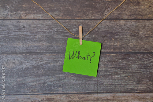 Green note hanging on a string against a wooden background; text: 