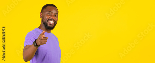 Canvastavla Smiling Black Man In His 30s Sitting Against Bright Yellow Background, Pointing At Camera With A Joyful Expression, Exuding Confidence And Positivity, Ideal For Business Concept Imagery