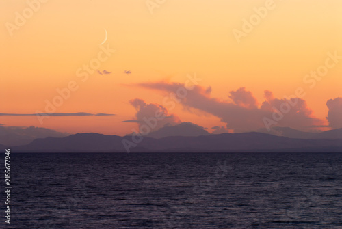Mare calmo al crepuscolo con luna crescente e scogli