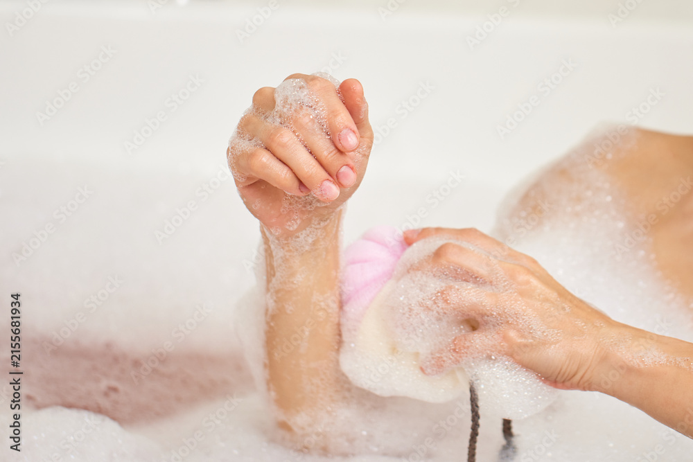 Fototapeta premium Woman washing arm with pink sponge in bubble bath