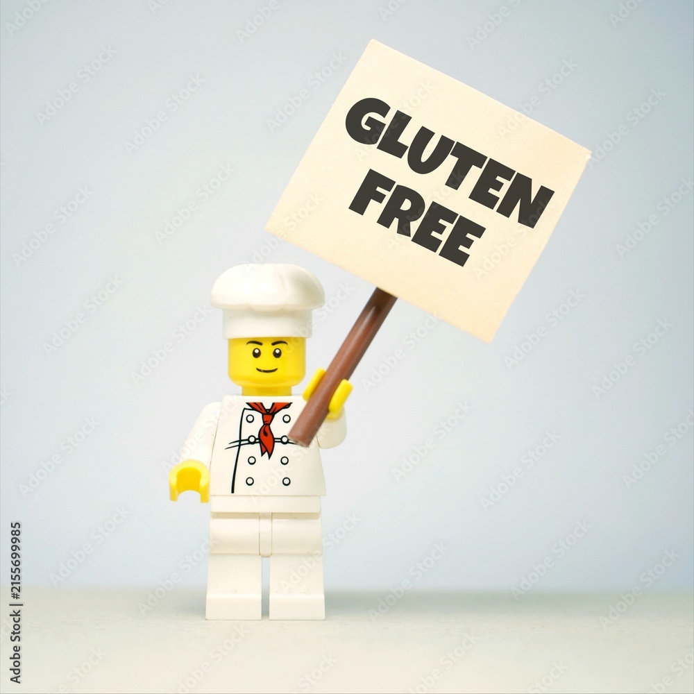 Obraz premium Indonesia - June 1, 2026 : Mini toy of action figure with blur background. Miniature photography concept design. Minifigure of people character hold GLUTEN FREE message text at poster banner.