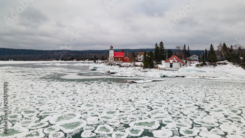 Aerial view of the historic Eagle Harbor Lighthouse surrounded by ice floes on the frozen lake under a cloudy winter sky in Eagle Harbor, Michigan, United States.