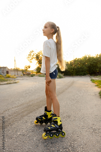 Fotografie A happy blonde girl is roller-skating along a park path at sunset