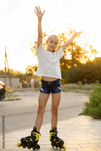 A happy child is having fun and posing on roller skates on a paved sidewalk 