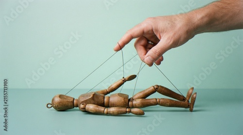 Foto A close-up shot of a human hand manipulating a wooden artist mannequin with strings against a plain pastel green background, representing control, influence, or helplessness