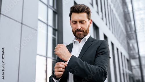 Quadro su tela Focused Caucasian Male Businessman Adjusting Cufflink At Professional Setting Outside Modern Office Building