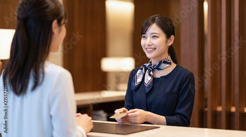 ホテルのフロントで笑顔でクレジットカードを受け取る女性スタッフと接客を受ける顧客