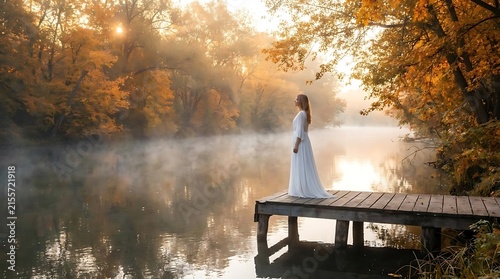 Woman on pier at misty autumn lake during sunrise.