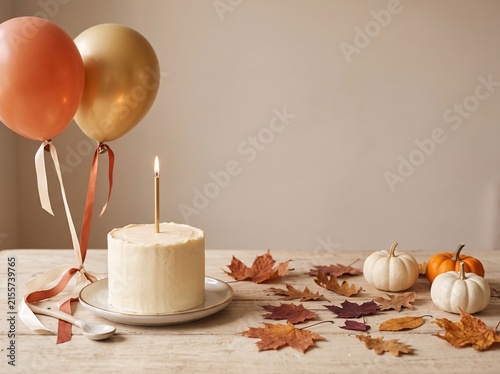 Elegant autumn birthday scene featuring a white cake, orange and gold balloons, pumpkins and colorful fall leaves arranged on a light neutral background. Perfect for birthday celebrations