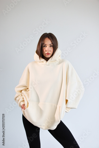 Young woman presenting empty cream hooded sweatshirt mockup, casual streetwear.