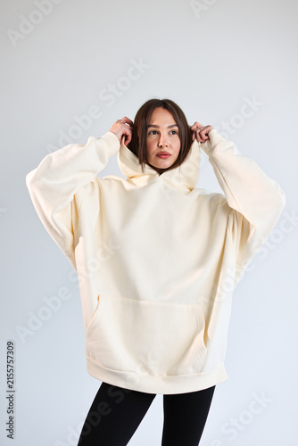Young woman presenting empty cream hooded sweatshirt mockup, casual streetwear.