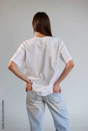 Back view of a female model in a blank white t-shirt mockup and jeans.