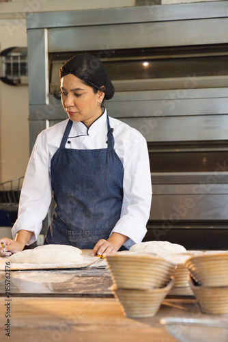 Mid adult African American woman in chef coat shaping dough at bakery bench with bannetons