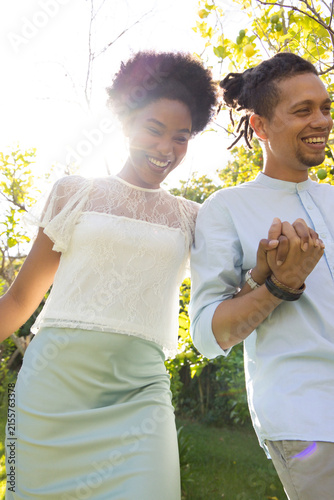 African American couple walking hand-in-hand in sunlit park, wearing lace blouse, bracelets