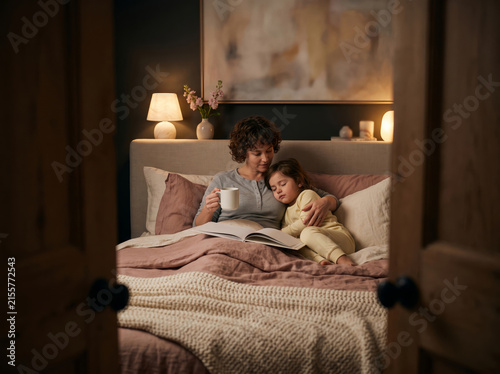 Parent and young child resting in bed with a book viewed through a doorway, representing family bonding and comforting bedtime routines.