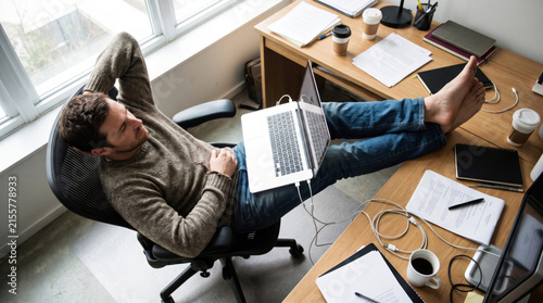Man resting laptop office desk chair work casual home office, overhead view of male freelancer relaxing with computer on lap near window and paperwork, calm remote work break
