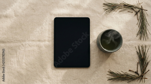 Flat lay of blank tablet and hot green tea on beige linen cloth.