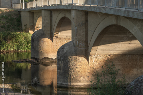 Dreiviertelansicht Neckarbrücke Rundbogenbrücke aus Sandstein mit halbrunden Strömungsteilern mit Spiegelung und Seitenlicht von tiefstehender Sonne in Neckartenzlingen.	

