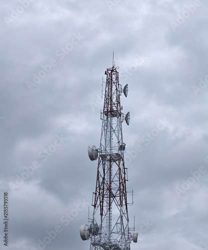 Fotografía Tall red and white telecommunications antenna tower with microwave dish antennas against cloudy overcast sky