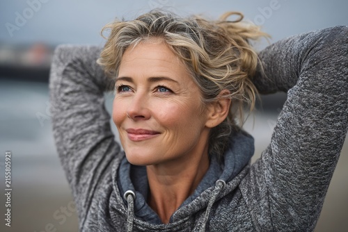 Middle-aged woman with beautiful blonde hair stretching outdoors by the invigorating seaside
