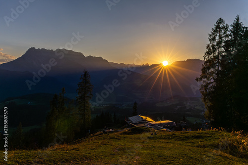 Spectacular golden sunrise behind mountain peaks with dramatic sunburst and alpine valley view