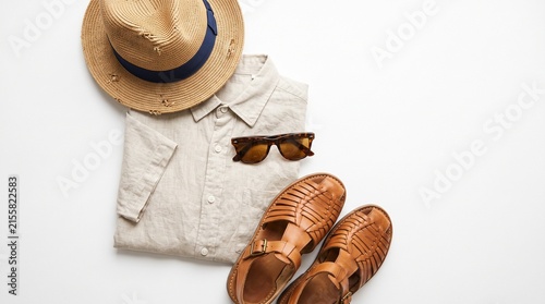 Vacation Essentials: A neatly folded linen shirt, a straw fedora hat, stylish sunglasses, and leather sandals arranged to evoke a sense of summer leisure and travel.