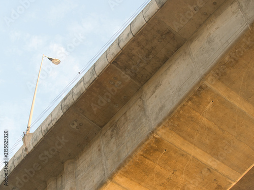 Low-angle view of a reinforced concrete bridge spanning a river an elevated highway structure set against a clear blue sky.