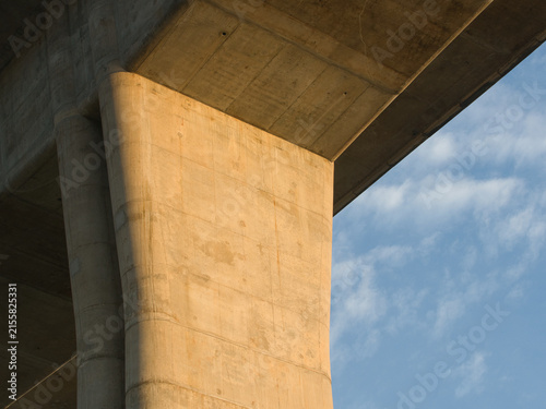 Low-angle view of a reinforced concrete bridge spanning a river an elevated highway structure set against a clear blue sky.