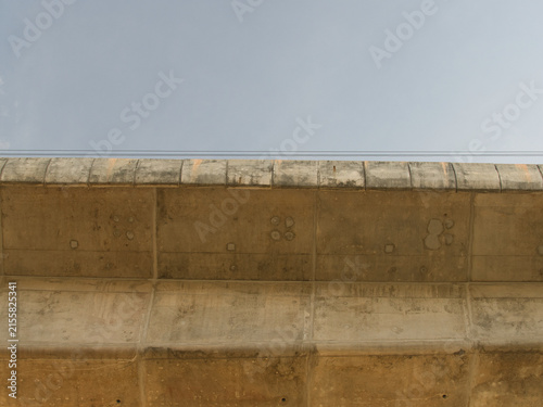 Low-angle view of a reinforced concrete bridge spanning a river an elevated highway structure set against a clear blue sky.