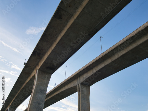 Low-angle view of a reinforced concrete bridge spanning a river an elevated highway structure set against a clear blue sky.