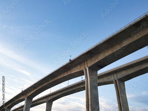 Low-angle view of a reinforced concrete bridge spanning a river an elevated highway structure set against a clear blue sky.