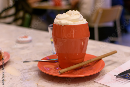 Canvastavla Taza naranja con bebida caliente y abundante crema batida sobre plato a juego y sorbete de papel en mesa de terrazo