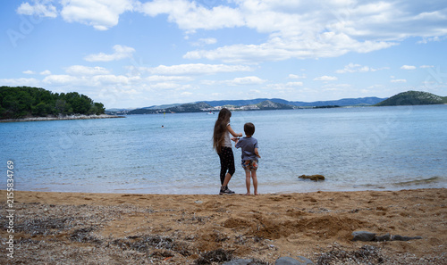 Two children standing on a sandy beach and looking at the sea on Vrgada island, Croatia
