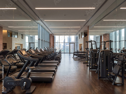 urban modern gym interior with treadmills and exercise machines in clean setting, featuring wooden flooring and metal frames, promoting fitness centers and urban living spaces.