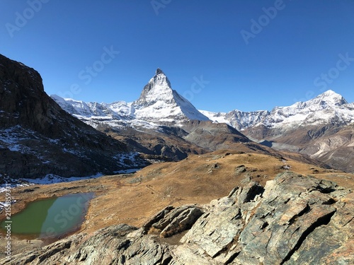 Принти на полотні Snow-covered Matterhorn reflected in a calm alpine lake beneath a clear blue sky near Zermatt in the Swiss Alps, Switzerland